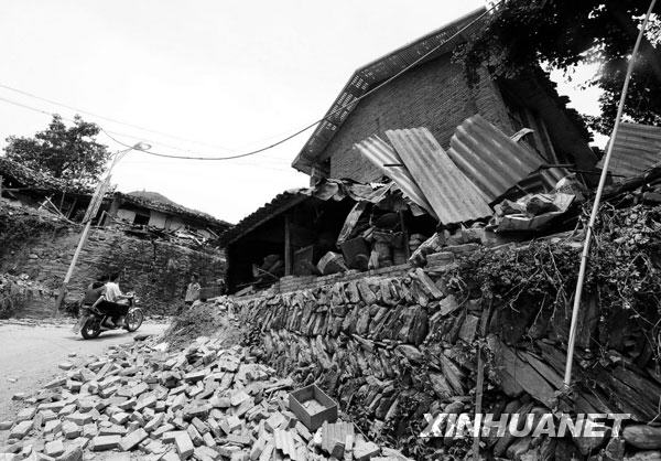 2008年5月15日，当地群众从甘肃省陇南市文县碧口地区三乡一镇地震灾区一处被震毁的房屋旁走过。