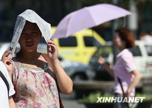 6月24日，一名郑州市民在街头用报纸遮挡烈日。